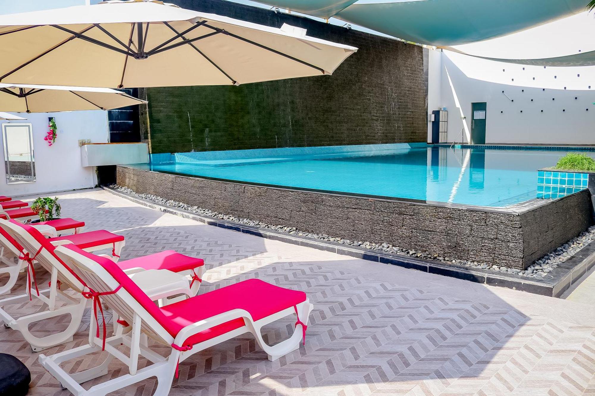 Lagoona Beach Luxury Resort And Spa Manáma Exteriér fotografie The photo shows a pool area featuring a rectangular swimming pool with clear blue water. Surrounding the pool are light-colored lounge chairs with pink cushions, positioned under large umbrellas for shade. The pool is bordered by a textured wall, and