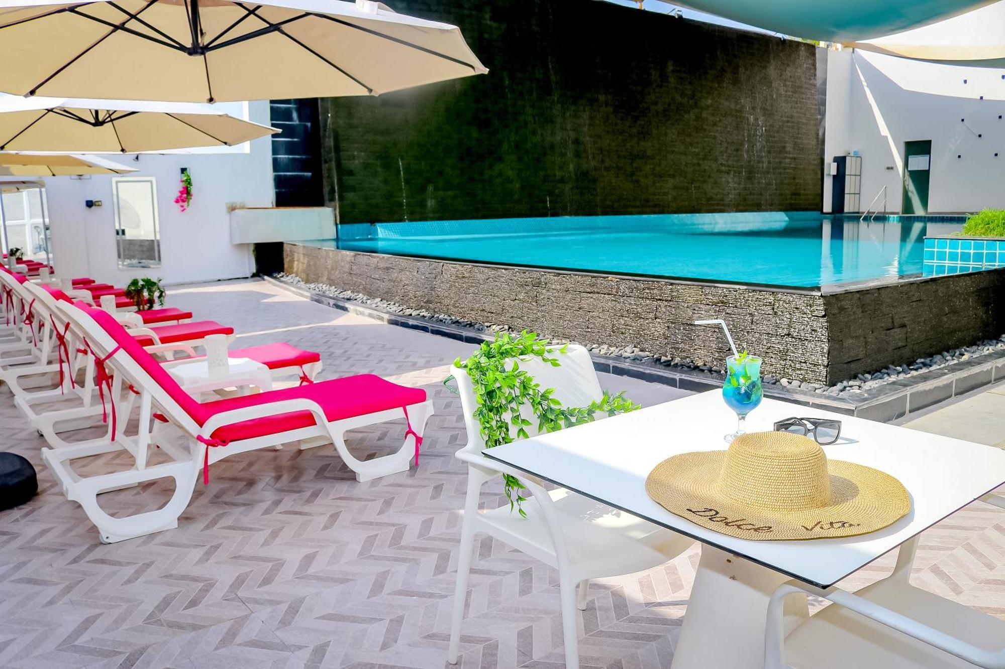 Lagoona Beach Luxury Resort And Spa Manáma Exteriér fotografie The photo shows a sunny poolside area with bright red lounge chairs arranged neatly beside a swimming pool. There are large beige umbrellas providing shade. A small table is set up with a straw hat and a colorful drink, suggesting a relaxed, tropical