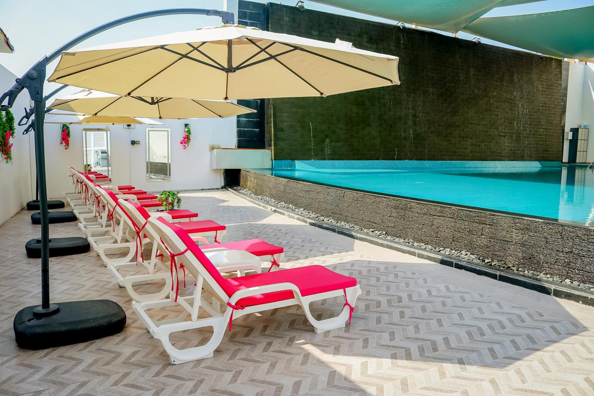 Lagoona Beach Luxury Resort And Spa Manáma Exteriér fotografie The photo shows a sunny poolside area with several lounge chairs arranged in a row. Each chair features red cushions and is positioned under large, beige umbrellas for shade. In the background, there is a beautiful swimming pool with clear blue water