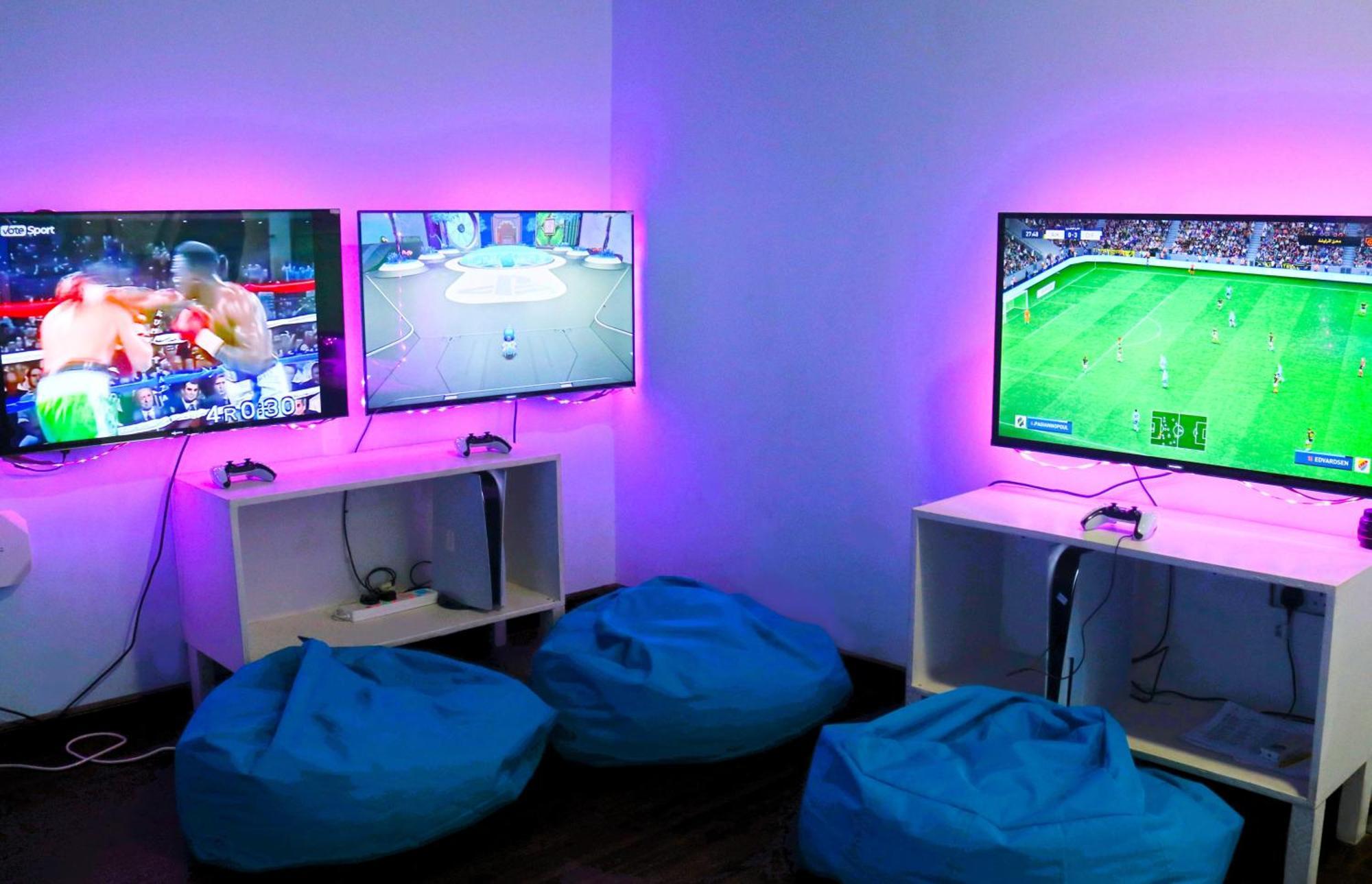 Lagoona Beach Luxury Resort And Spa Manáma Exteriér fotografie The photo shows a gaming area featuring three televisions mounted on the wall, displaying different games. Two of the TVs are showing gaming scenes, with one depicting a boxing game and the other showing a vibrant game environment. The third TV displ