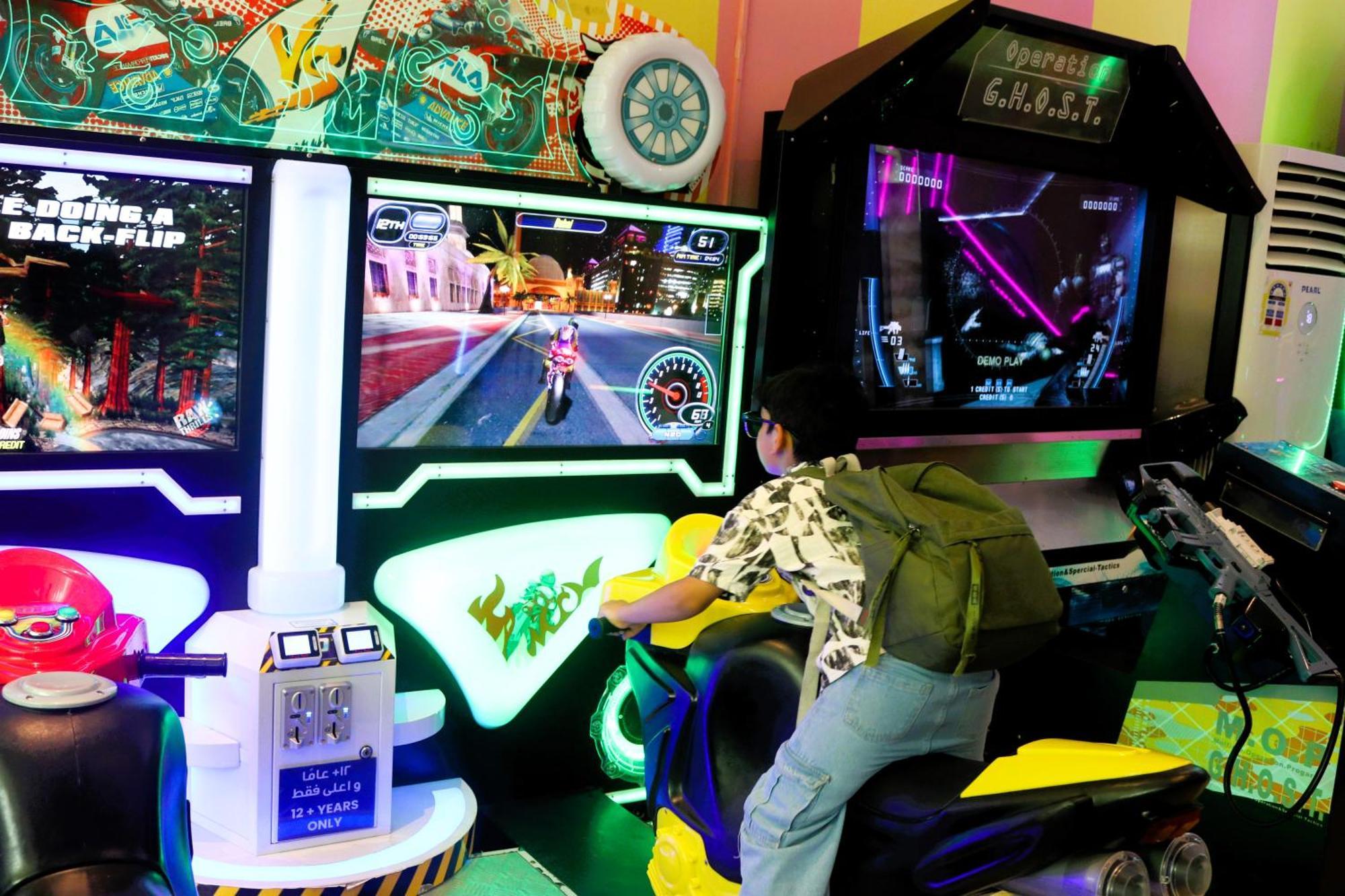 Lagoona Beach Luxury Resort And Spa Manáma Exteriér fotografie The photo shows a person playing an arcade motorcycle racing game. They are seated on a motorcycle-shaped seat, actively engaging with the game displayed on the screen in front of them. The screen shows a vibrant racing scene with streets and colorfu