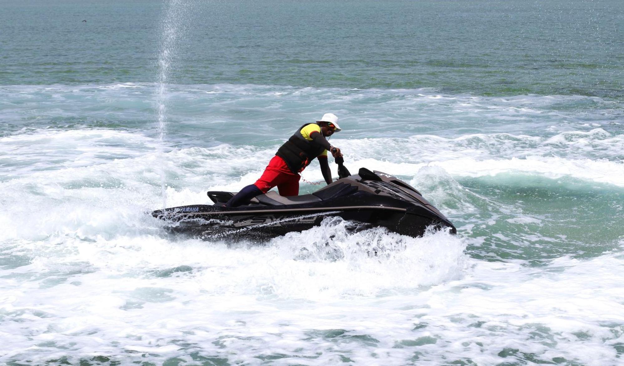 Lagoona Beach Luxury Resort And Spa Manáma Exteriér fotografie The photo shows a person riding a jet ski on the water. The rider is positioned upright, leaning forward with one hand on the handlebars, while the jet ski creates splashes of white foam around it. The water appears choppy, likely due to the motion o