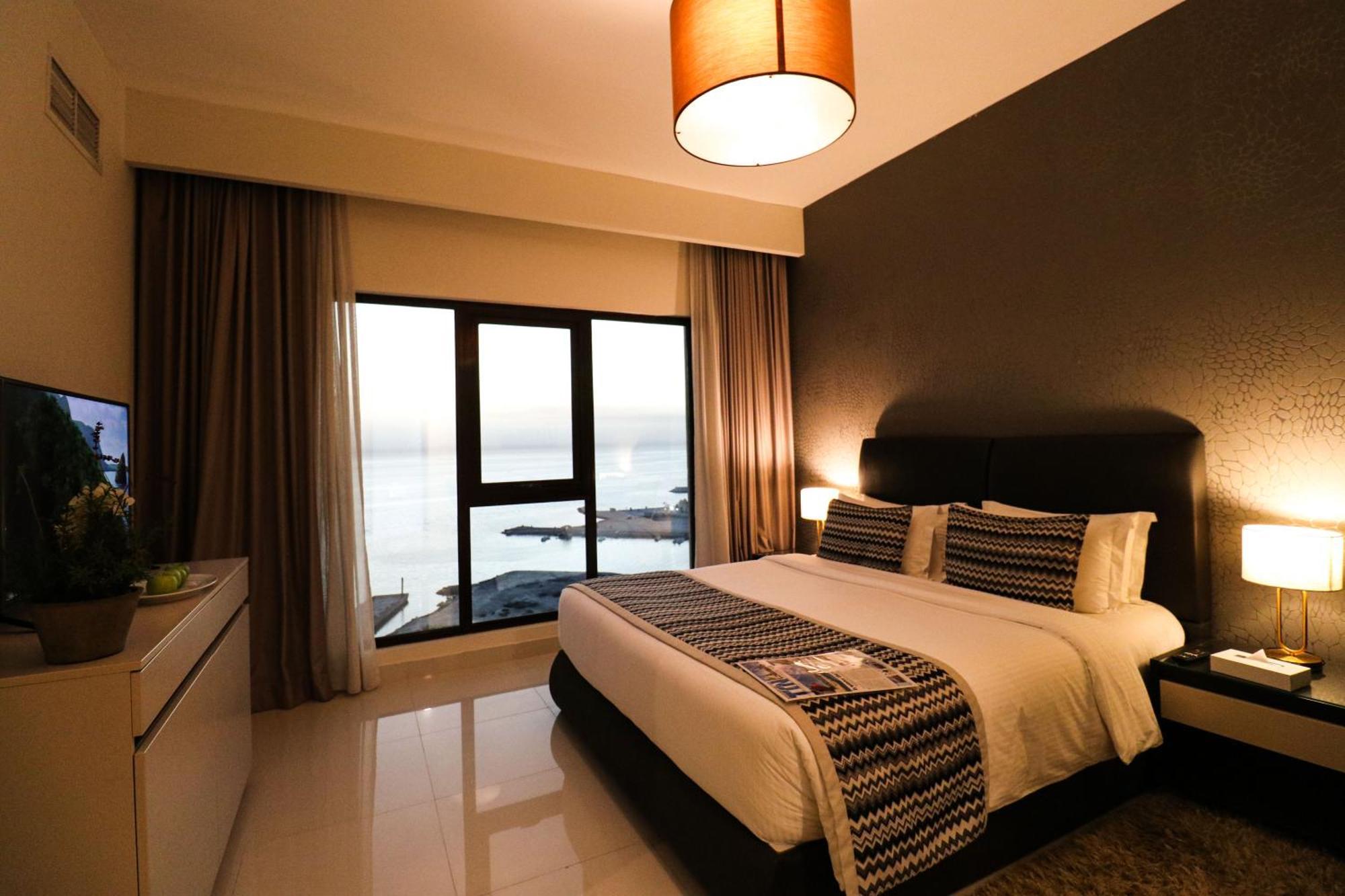 Lagoona Beach Luxury Resort And Spa Manáma Exteriér fotografie The photo shows a modern hotel room featuring a neatly made bed with decorative pillows. The room has a stylish design with a dark accent wall and a large window that offers a view of the outdoors. Natural light comes in, giving the space a bright an