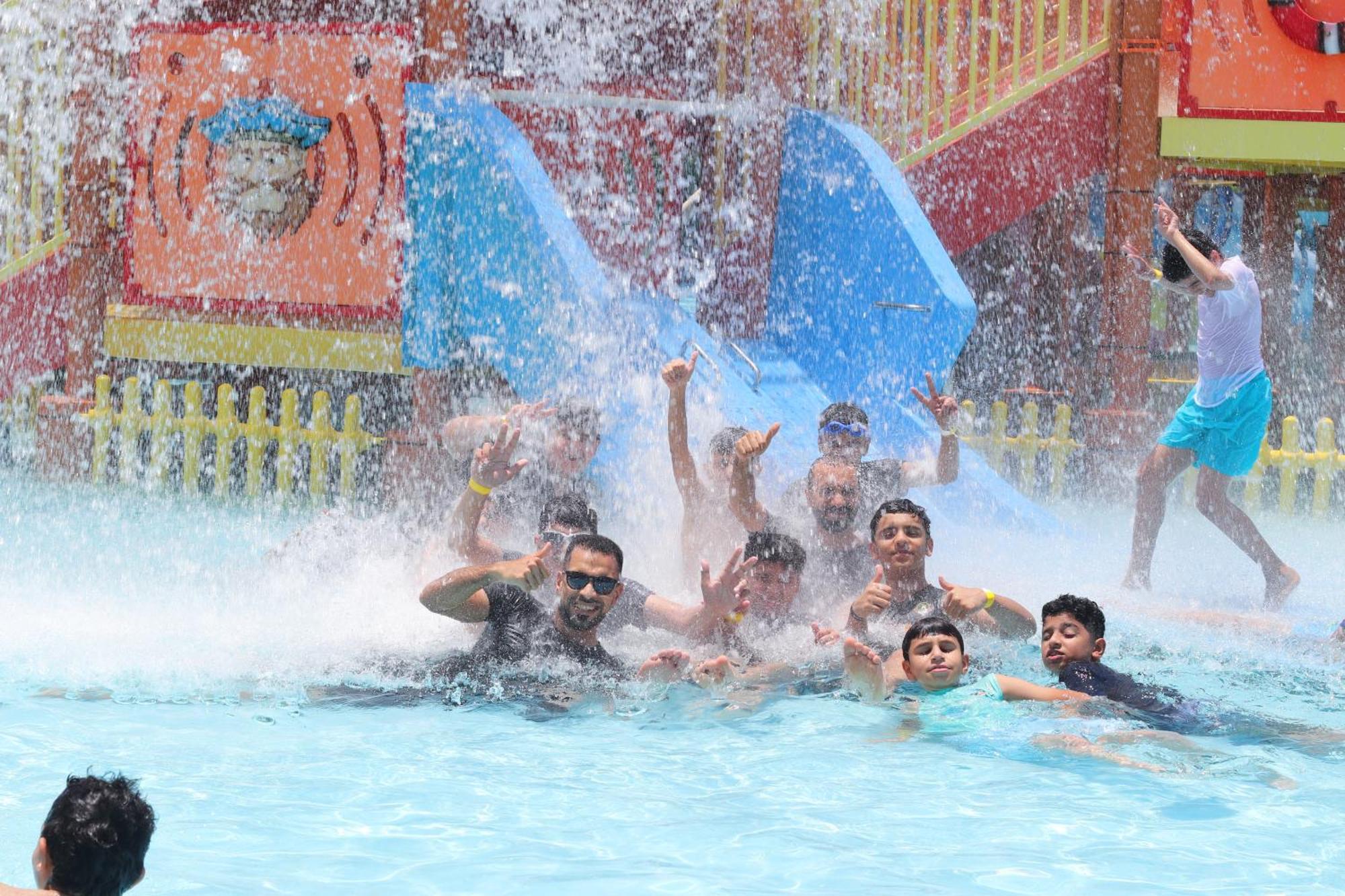 Lagoona Beach Luxury Resort And Spa Manáma Exteriér fotografie The photo shows a lively scene at a water park or pool area. Several people, including adults and children, are enjoying themselves in the water, splashing and posing for the camera. Water is cascading down, creating a refreshing atmosphere. In the b