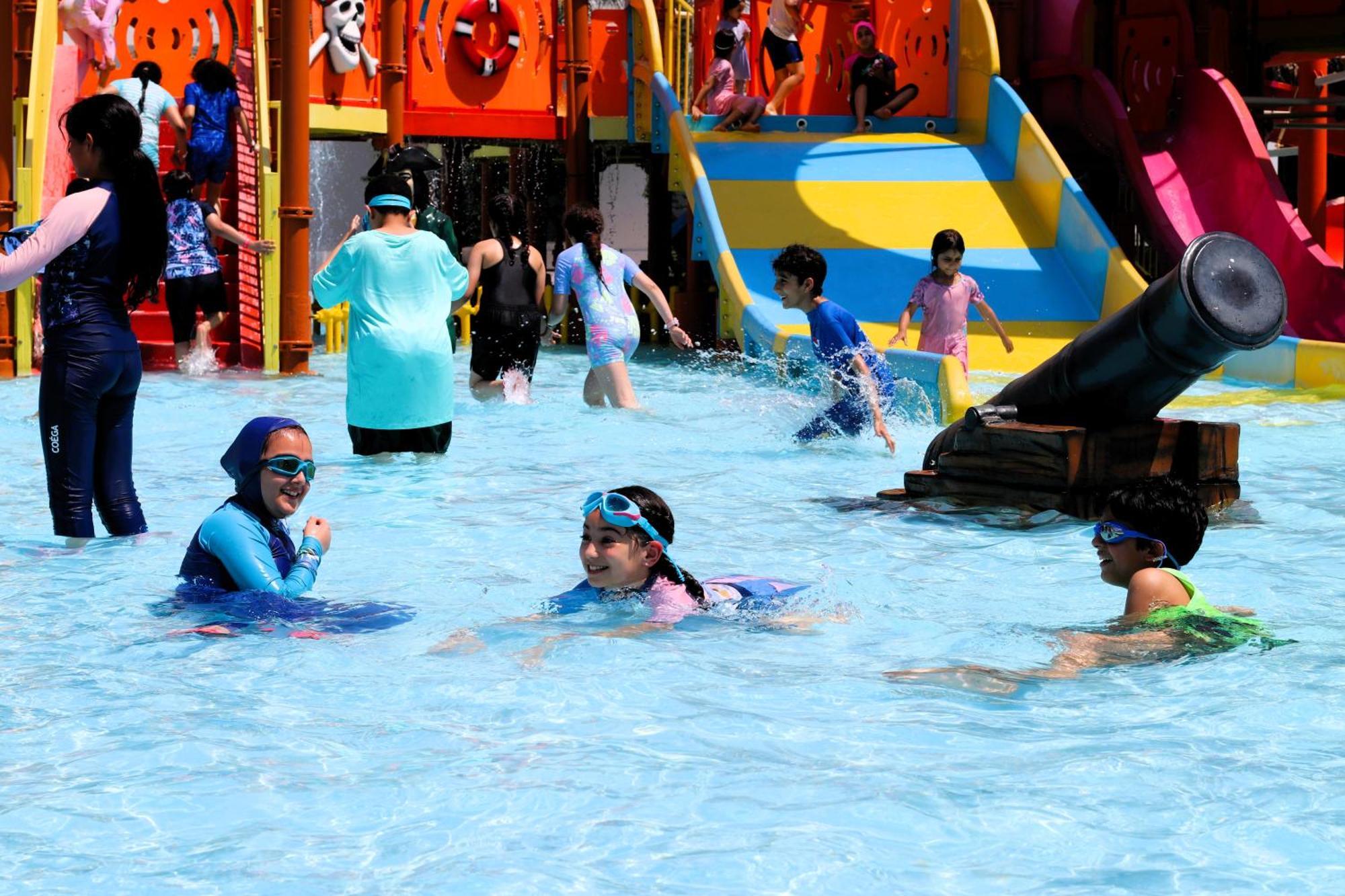 Lagoona Beach Luxury Resort And Spa Manáma Exteriér fotografie The photo shows a vibrant water park scene with several children playing in a shallow pool. Some are swimming and splashing around, while others are playing on colorful slides in the background. The atmosphere is lively and cheerful, with kids of var