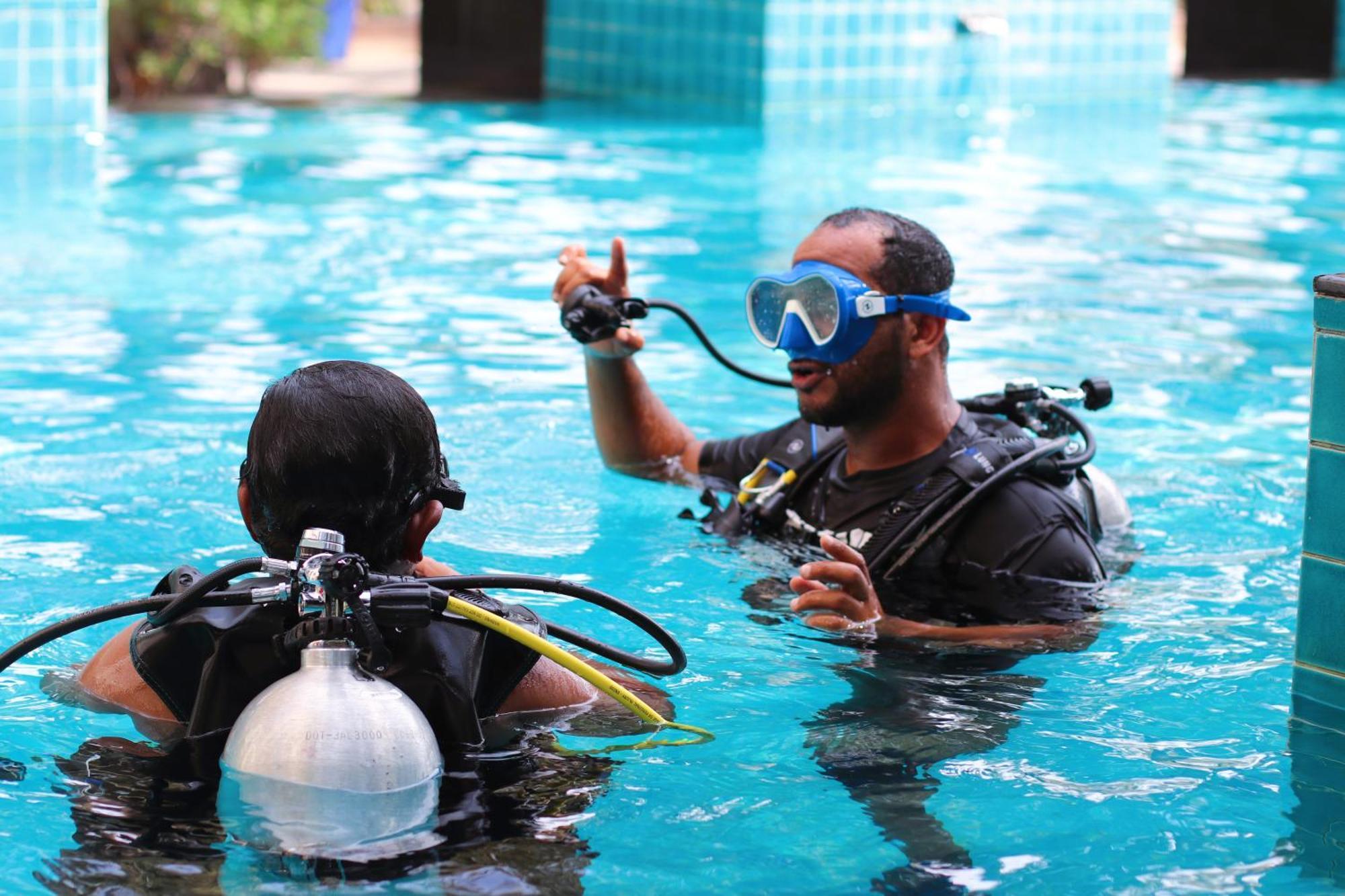 Lagoona Beach Luxury Resort And Spa Manáma Exteriér fotografie The photo shows two divers in a pool. One diver is wearing a scuba mask and is speaking to the other diver, who is also equipped with scuba gear. They appear to be engaged in a discussion, possibly related to diving instructions or safety. The water 