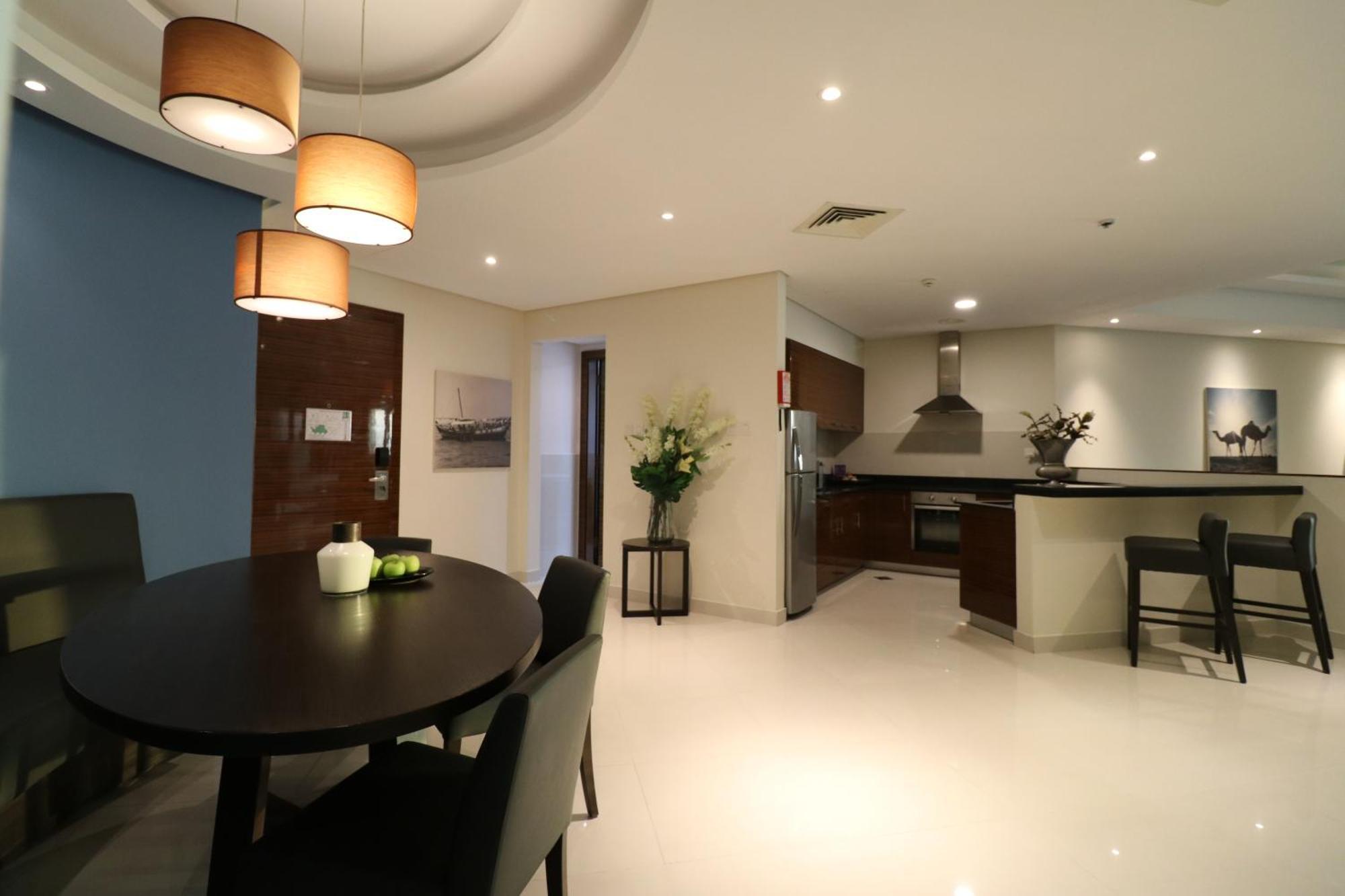 Lagoona Beach Luxury Resort And Spa Manáma Exteriér fotografie The photo shows a modern, open-concept dining and kitchen area. On the left, there is a round dining table with black chairs, accompanied by a few decorative elements like a small vase and some fruit. The walls have a combination of light and dark to