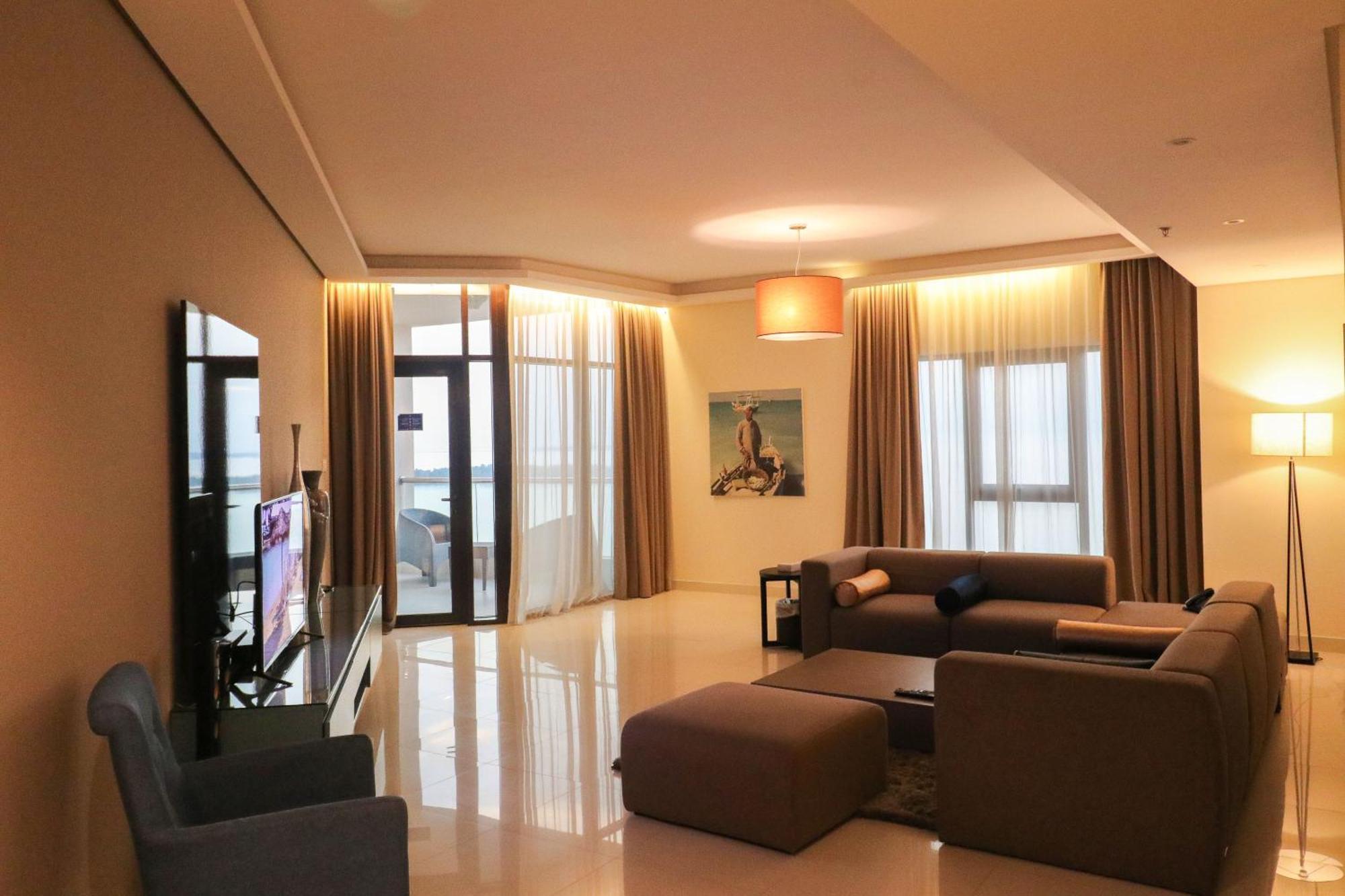 Lagoona Beach Luxury Resort And Spa Manáma Exteriér fotografie The photo shows a modern living room with a spacious and elegant design. It features a large couch in neutral tones, a soft ottoman, and a stylish coffee table. The walls are painted in a light color, and there are large windows with sheer curtains a