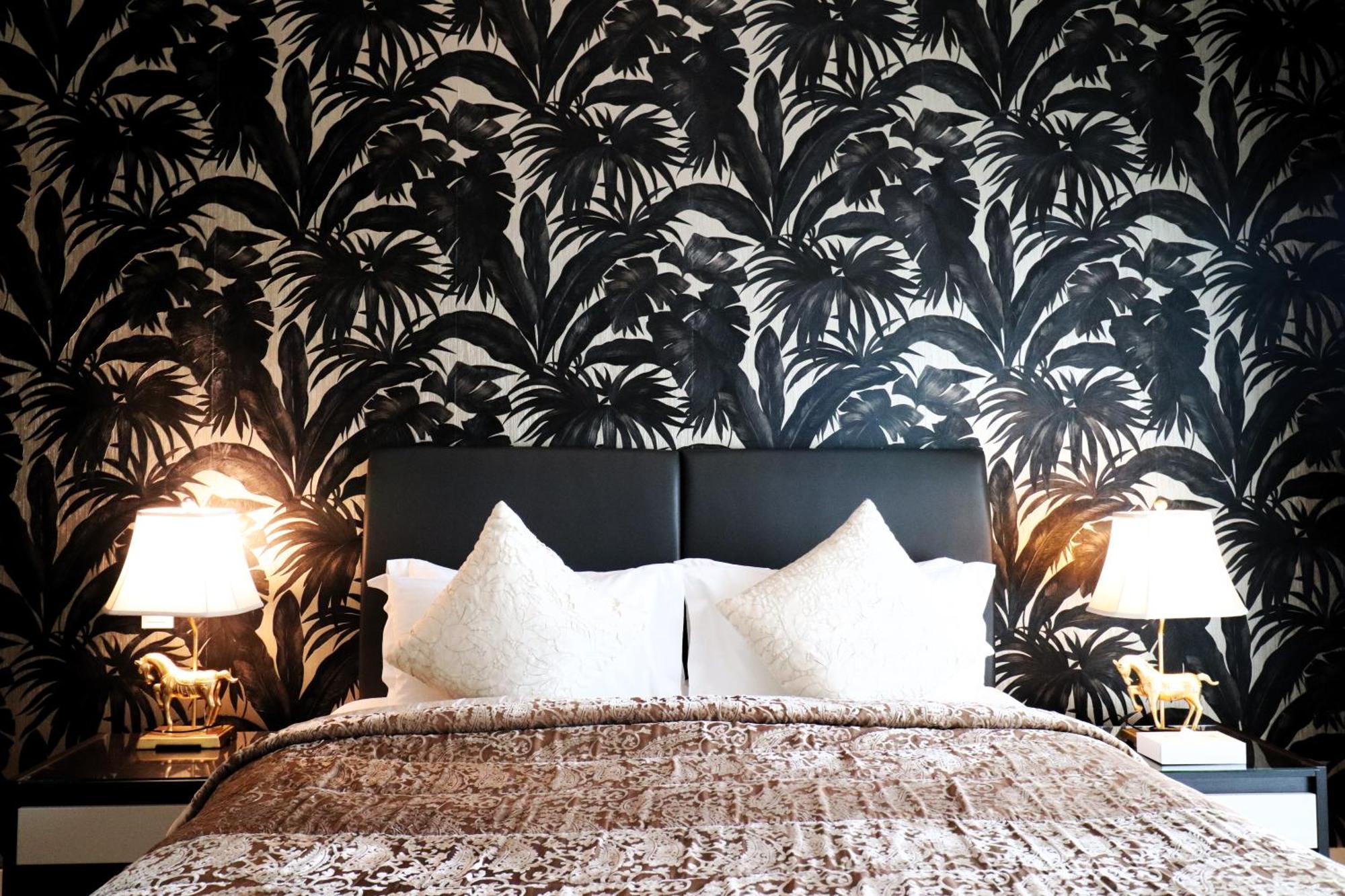 Lagoona Beach Luxury Resort And Spa Manáma Exteriér fotografie The photo depicts a stylish bedroom featuring a distinctive wall covered in a black and white tropical foliage wallpaper. The bed has a modern black headboard and is adorned with white pillows, creating a clean and elegant look. A textured brown thro