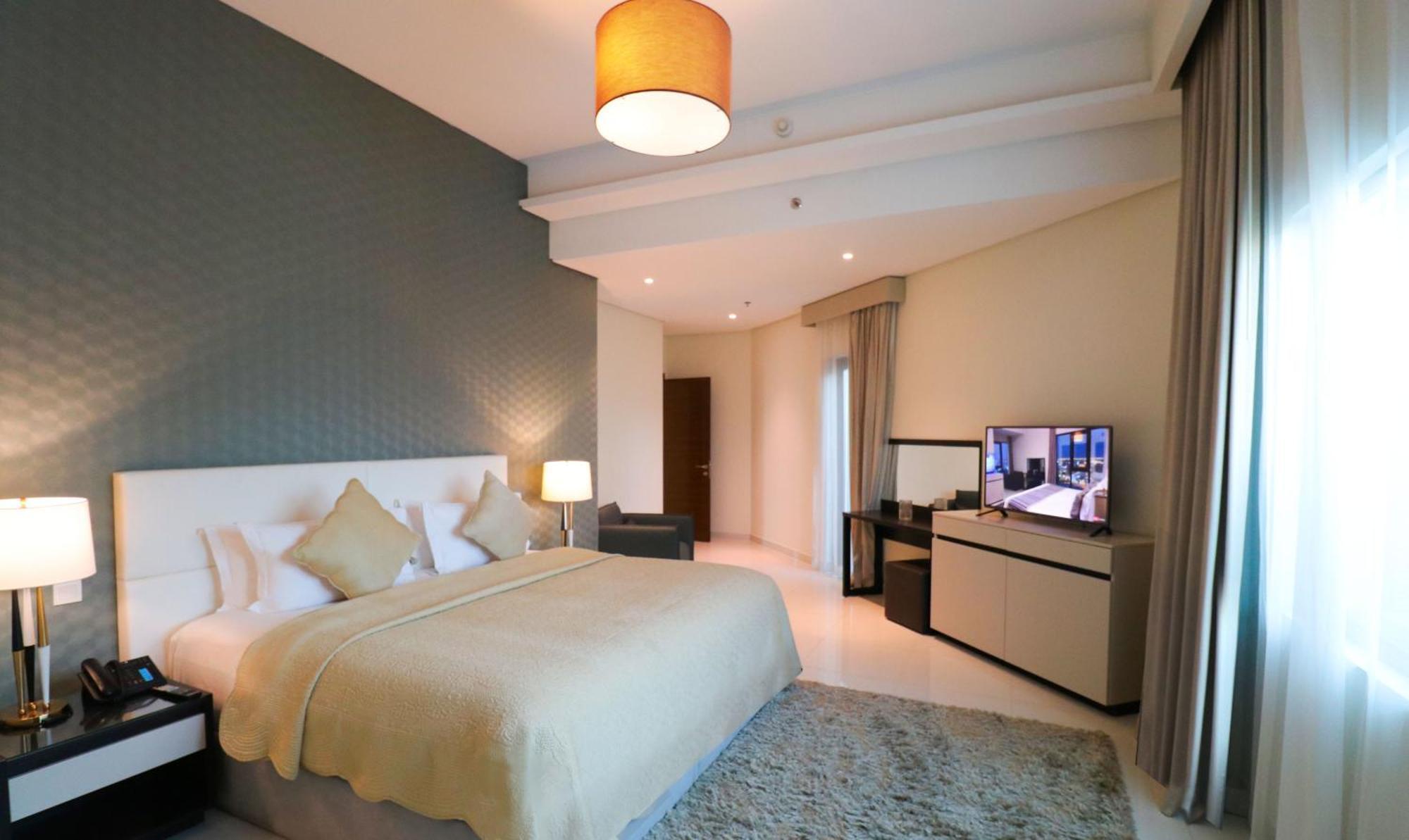 Lagoona Beach Luxury Resort And Spa Manáma Exteriér fotografie The photo shows a modern hotel room featuring a large bed with a light-colored blanket and decorative pillows. The walls are painted in a subtle shade, and there is a textured accent wall behind the bed. On one side, a bedside lamp provides warm ligh