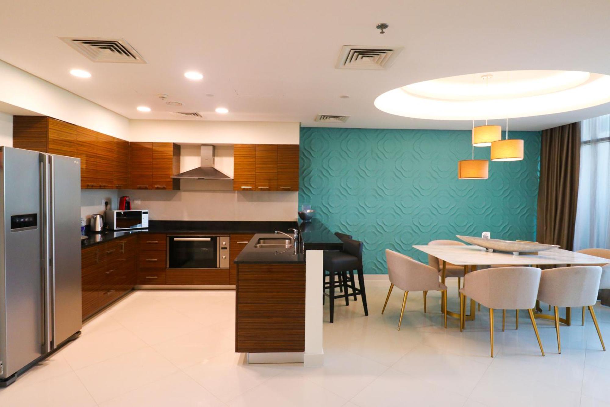 Lagoona Beach Luxury Resort And Spa Manáma Exteriér fotografie The photo shows a modern kitchen and dining area. The kitchen features wooden cabinets, sleek appliances including a stainless steel refrigerator, microwave, and an oven. There is a dark countertop and a small breakfast bar with high stools. The wall